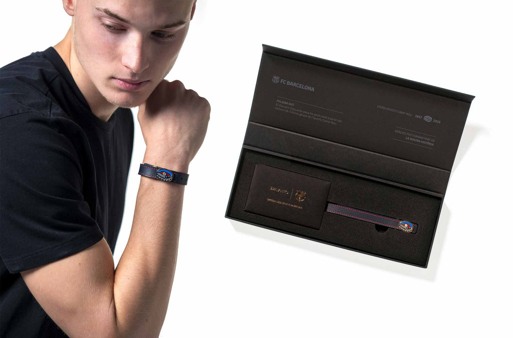 Modelo nórdico con camiseta corta de color negro luciendo la pulsera 1957 del FC Barcelona, con un diamante de 0.10 quilates y de alta joyería junto a el packaging de la pulsera, una caja imantada negra premium con acabados dorados.